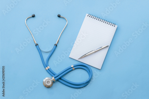 Cardiologist's day; doctor's day; heart disease; Cardiology, blue stethoscope with notebook and pen on a blue background; diagnosis of heart disease; happy cardiologist's day