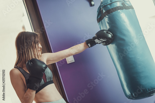 Young female boxer punching a boxing bag at gym, doing strength training