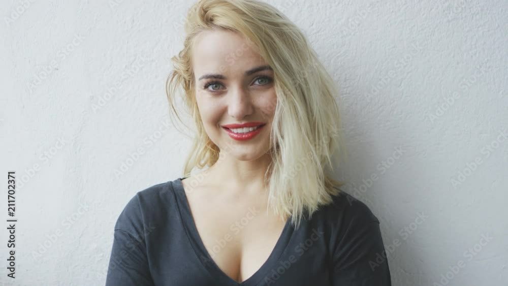 Happily smiling gorgeous blond woman in black casual shirt standing relaxed at white wall and looking at camera Happily smiling gorgeous blond woman in black casual shirt standing relaxed at white wall and looking at camera