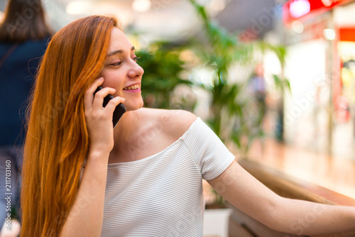 Young redhead pretty girl in a shopping center keeping a conversation with the mobile phone with someone