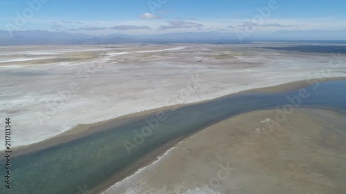 Aerial drone scene of Llancanelo lagoon in Malargüe, Mendoza, Argentina. Water reflection and white dry salty shore ground. Camera moving forwards towards a volcano. The Andes mountains on background photo