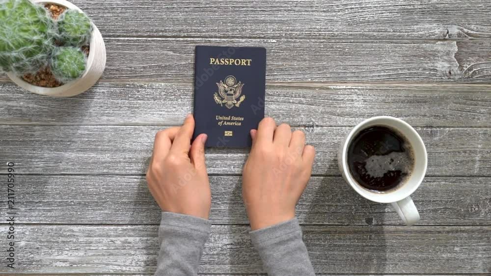 Person placing an American passport on a wooden desk Person placing an American passport on a wooden desk