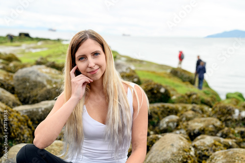 Young woman sitting on rock and smiling friendly into the camera in the intertidal zone of Vancouver, British Columbia