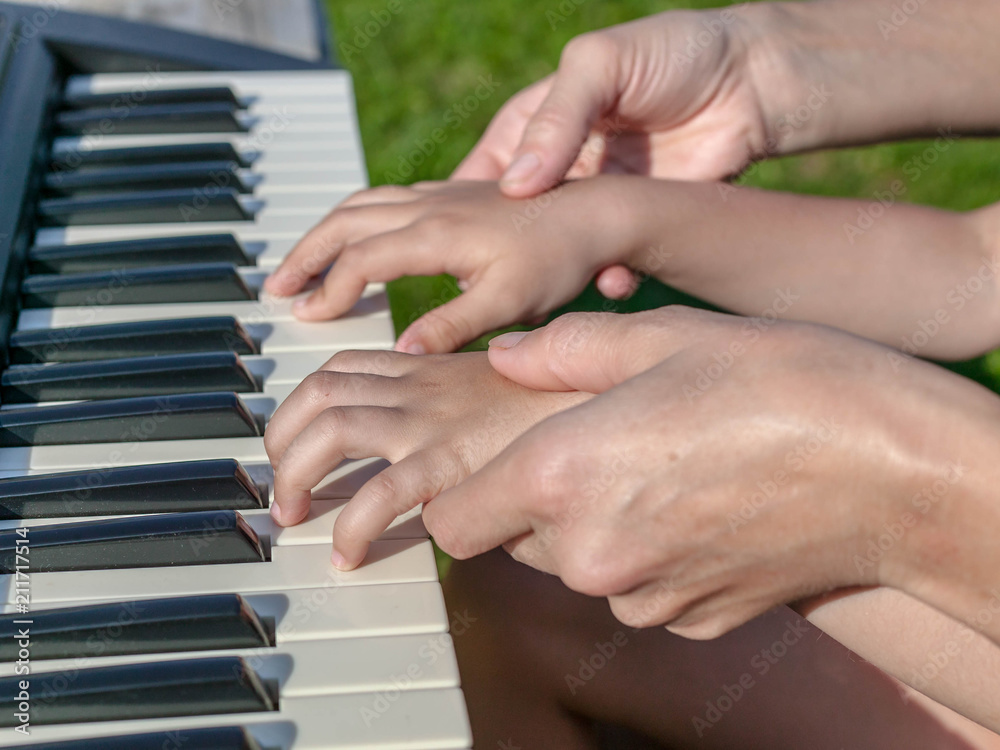 Fototapeta premium Mother teaches the daughter to play the piano. Concept Mother's Day. Female and children's hands.