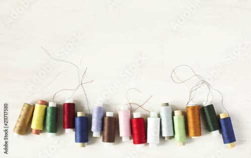 Colourful thread spools on a white wooden background with copy space