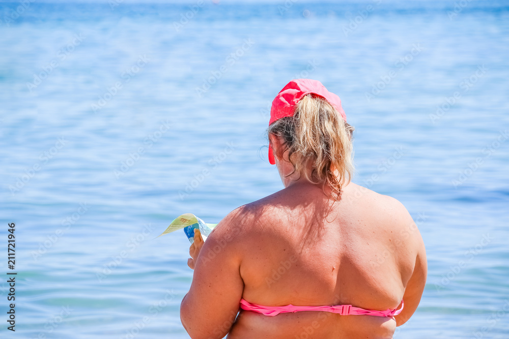 mature woman in swimwear at the sea. Overweight woman in swimsuit comes on  the beach, reading a book, rear view.Fat women sitting on a beach by an  ocean Stock Photo | Adobe