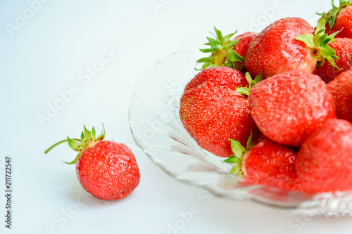 Red ripe strawberry with green leaves in a transparent glass plate on a light background