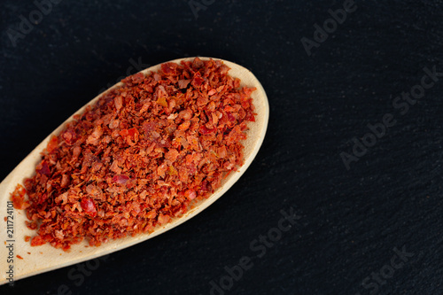 Red ground ground hot bitter pepper piled on a wooden spoon Dark black stone background
