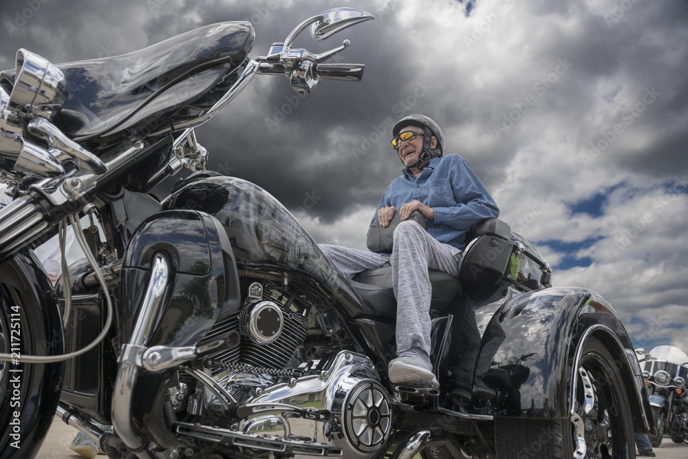 Fototapeta premium Elderly man sits on the back of a fancy three-wheeled motorcycle on a dark, stormy day 
