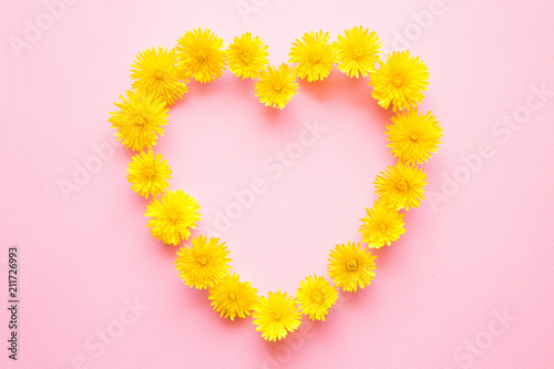 Heart shape is created from bright yellow dandelion heads on light pastel pink background. Love concept. Mockup for positive ideas. Empty place for delicate, emotional or sentimental text or quote.