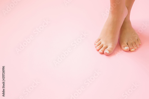Young, perfect groomed woman's feet on pastel pink background. Care about nails and clean, soft, smooth body skin. Pedicure and manicure beauty salon. Copy space. Empty place for text or logo.
