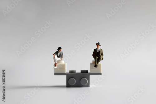 The concept of equality of opportunity for men and women. A miniature man and woman sitting on a mini seesaw. photo