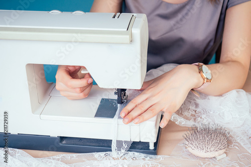 close-up hands of seamstress tailor ( dressmaker) thread the needle on the sewing machine on a blue background in the studio. The concept of creating a new collection of clothes photo