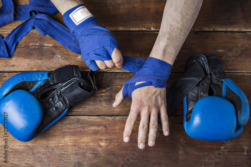 Process of taping male hands before of a boxing match on a wooden background. Boxing gloves lie on the table. Concept of boxing is learning or fighting. Flat lay, top view