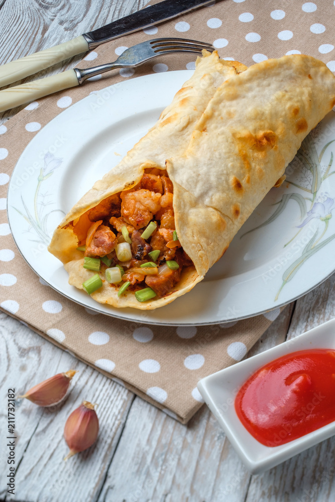 Doner kebab is lying on a white plate. Shawarma with meat, onions, salad lies on a white old wooden table. Doner kebab is lying on a white plate. Shawarma with meat, onions, salad lies on a white old wooden table.