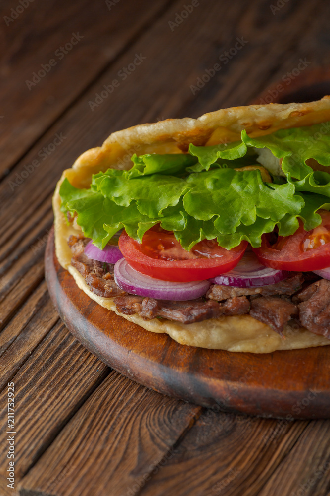 Delicious fresh homemade sandwich with chicken burspit roasted meat, tomato, onions and lettuce on wooden board on dark wooden table. Doner kebab. Healthy food concept. Delicious fresh homemade sandwich with chicken burspit roasted meat, tomato, onions and lettuce on wooden board on dark wooden table. Doner kebab. Healthy food concept.