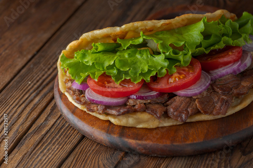 Delicious fresh homemade sandwich with chicken burspit roasted meat, tomato, onions and lettuce on wooden board on dark wooden table. Doner kebab. Healthy food concept.