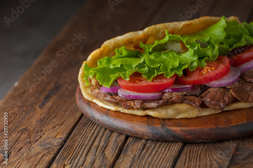 Delicious fresh homemade sandwich with chicken burspit roasted meat  tomato  onions and lettuce on wooden board on dark wooden table. Doner kebab. Healthy food concept.