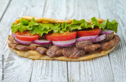 Delicious fresh homemade sandwich with chicken burspit roasted meat, tomato, onions and lettuce on wooden board on white wooden table. Doner kebab. Healthy food concept.