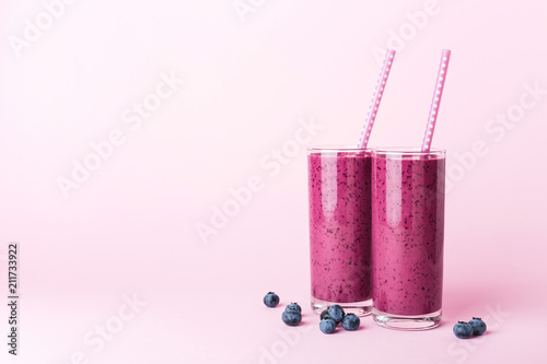 Two glasses of blueberries smoothie with straws on pink background. Healthy summer drink.