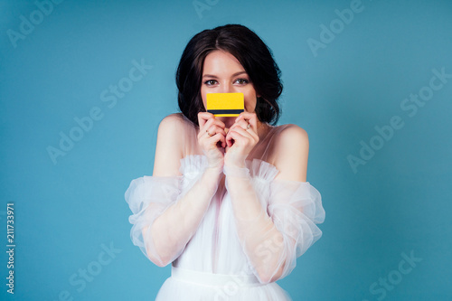 the bride in a wedding dress holds a credit card in her hand on a blue background in the studio