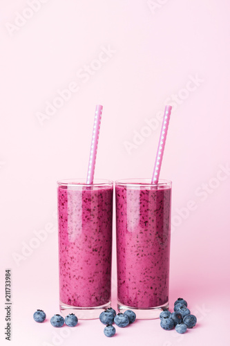 Fotografie Two glasses of blueberries smoothie with straws on pink background