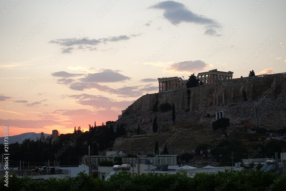 Iconic Acropolis hill and the Parthenon as seen from rooftop at sunset with golden colours and beautiful cloud formations, Athens historic center, Attica, Greece     