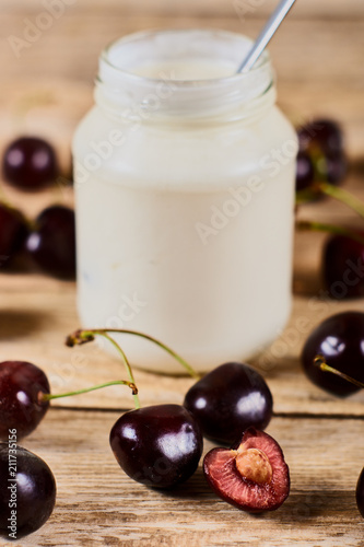 Greek yoghurt with spoon, opened cherry with a ossicle, on a cherryes and brown wooden background photo