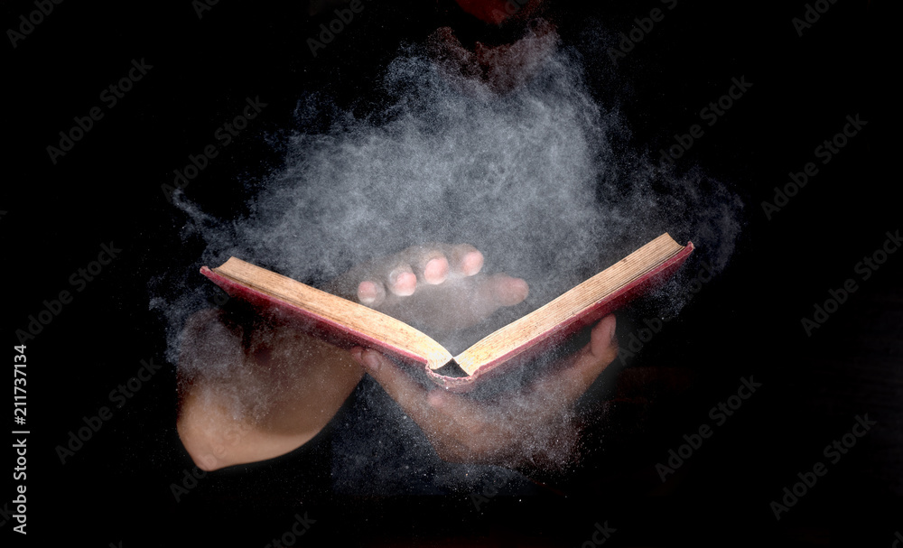 Fototapeta premium hand holding mysterious old book, white particle and smoke spread from book