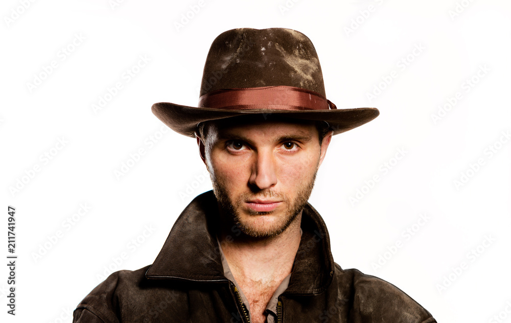 Young sexy  unshaven man in cowboy hat. Indiana Jones image. Stylish dark brown clothes on a white background