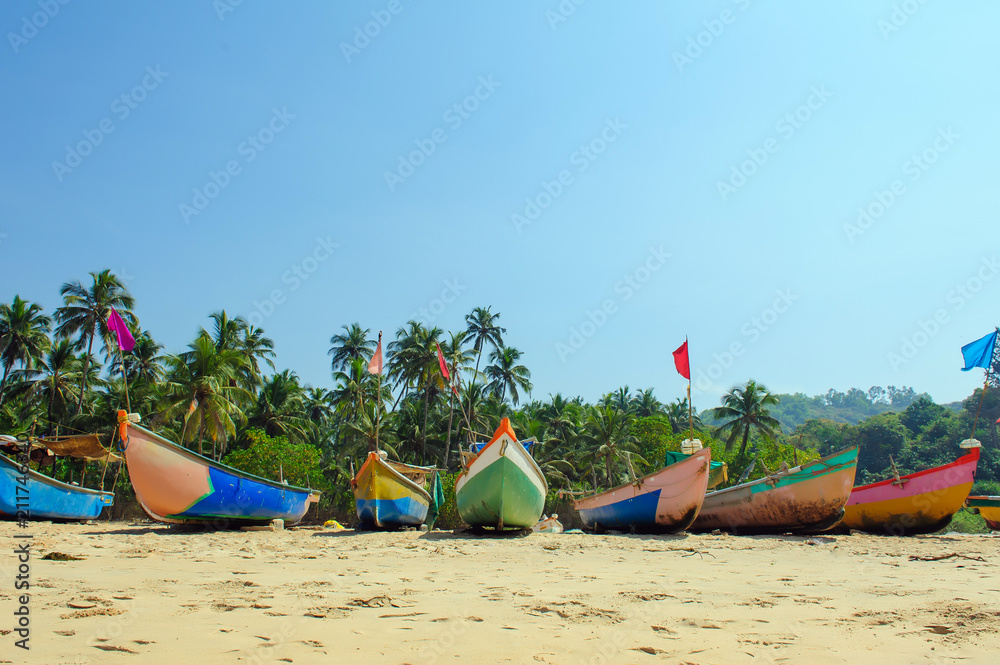 Small fishing boats in reggae colors on ocean beach seashore against blue sky. India, Goa, Maharashtra Small fishing boats in reggae colors on ocean beach seashore against blue sky. India, Goa, Maharashtra