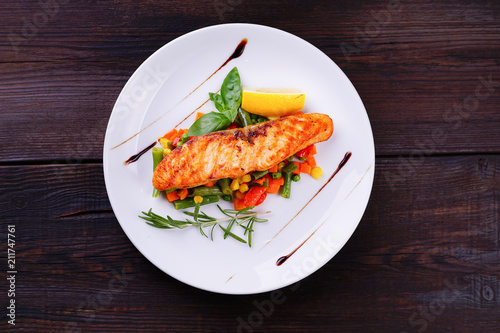 Delicious grilled salmon steak with vegetable garnishing, flat lay. Restaurant seafood menu photo, property nutrition and healthy food concept