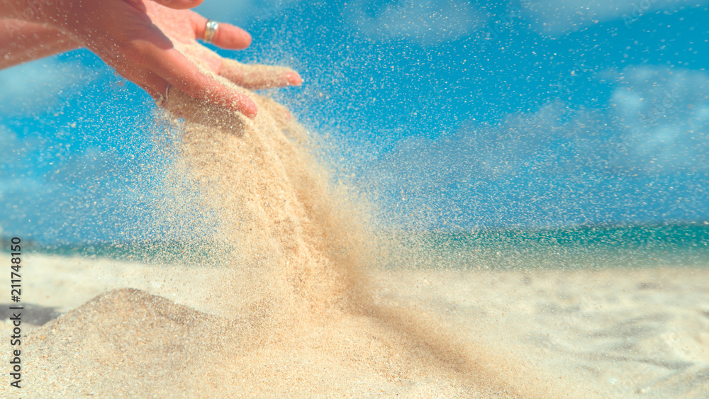 CLOSE UP: Unknown woman lets sand fall from her hands and back on the shore.