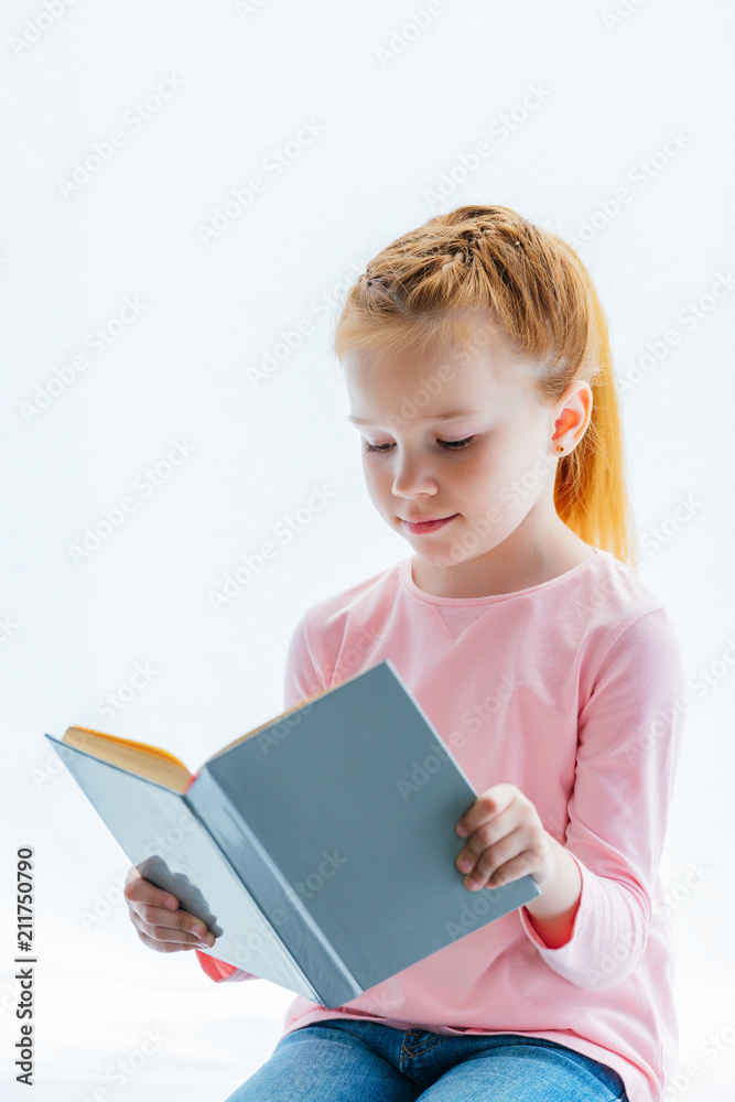 adorable red haired kid reading book while sitting on windowsill adorable red haired kid reading book while sitting on windowsill