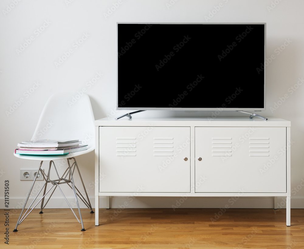 Wide screen TV on white stand near light wall