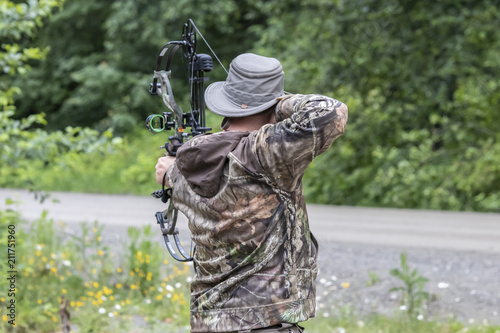 A Man Wearing Camouflage Shooting a Compound Bow  photo