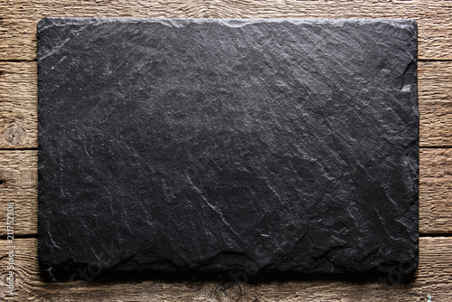 Black slate board on grunge wooden table closeup. Natural texture. Can be used like food background