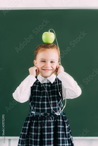 adorable little schoolgirl with apple on head and earphones smiling and looking at camera © LIGHTFIELD STUDIOS