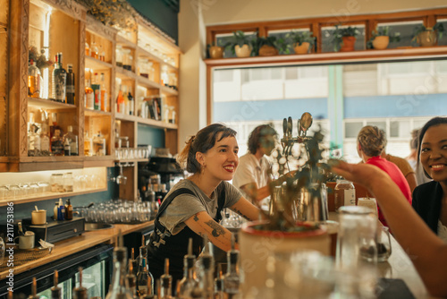 Smiling female bartender talking with customers at a bar counter photo
