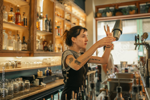 Young female bartender mixing cocktails behind a bar counter photo