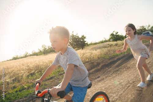 Boy and girl in the field. The boy is riding a bicycle, and the girl is running alongside. A cheerful, happy childhood in the village. photo