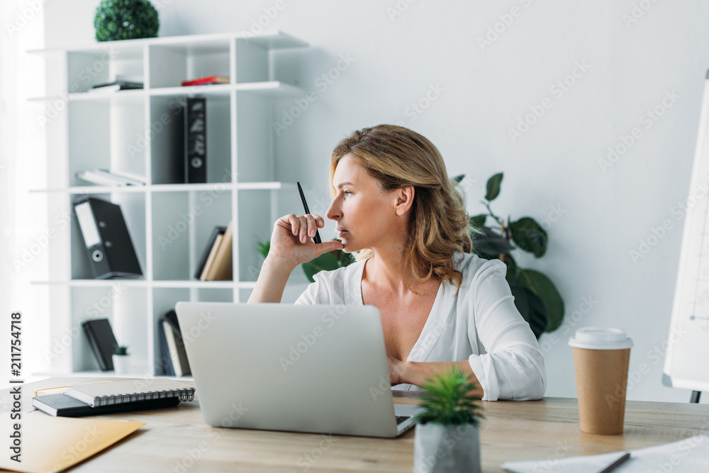 side view of attractive businesswoman sitting at table with laptop in office side view of attractive businesswoman sitting at table with laptop in office