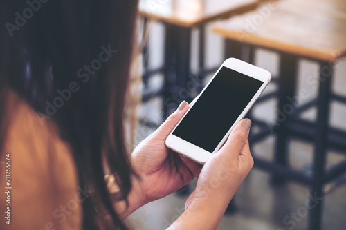 Mockup image of a woman holding white mobile phone with blank black desktop screen in cafe