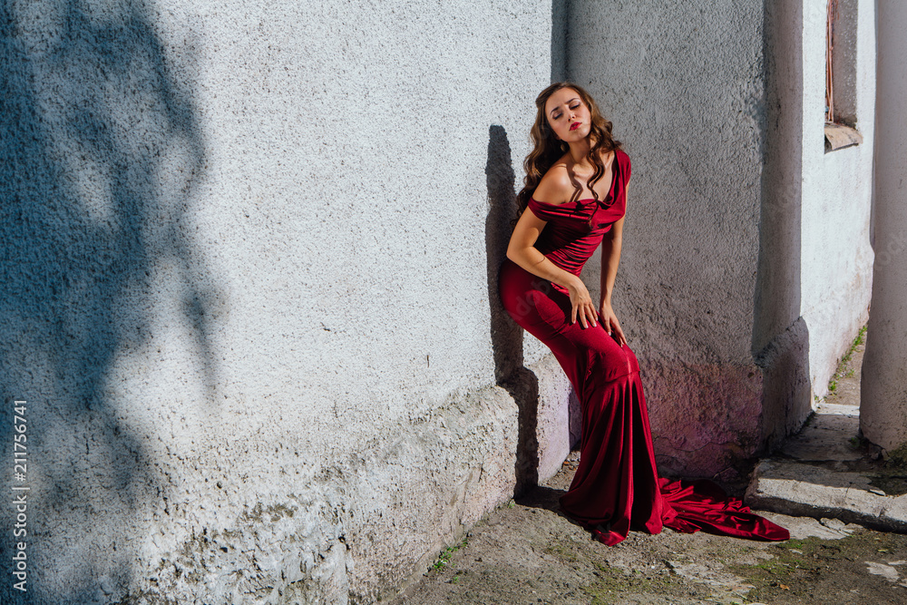 Beautiful young woman in a long red evening gown with a train Beautiful young woman in a long red evening gown with a train