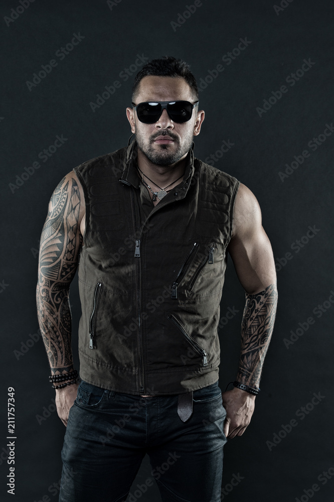 Tattoo model with beard on unshaven face. Bearded man with tattoo on strong arms. Tattooed man with biceps and triceps. Fashion macho in trendy sunglasses. Fashion style and trend, vintage filter Tattoo model with beard on unshaven face. Bearded man with tattoo on strong arms. Tattooed man with biceps and triceps. Fashion macho in trendy sunglasses. Fashion style and trend, vintage filter