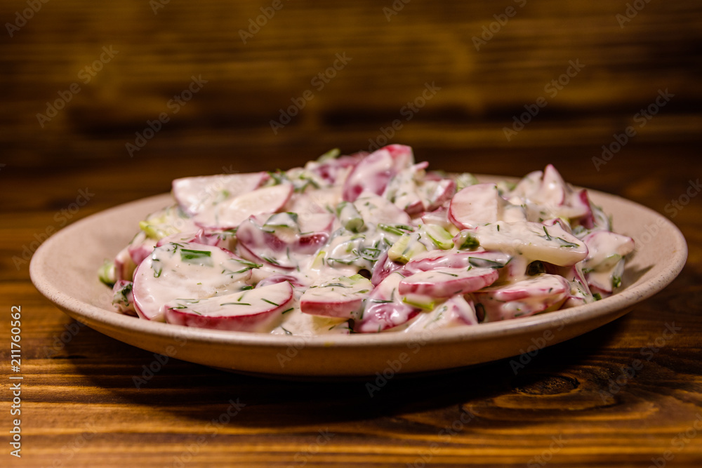 Vegetarian salad with radish, green onion and sour cream on a ceramic plate