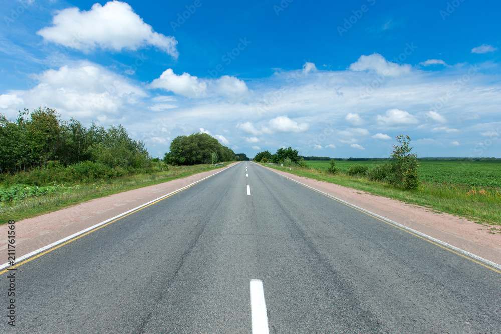 road through the green field and clouds on blue sky in summer day road through the green field and clouds on blue sky in summer day