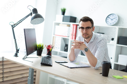 A young man in glasses stands near a table in the office. photo