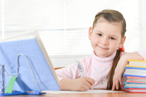 Cute schoolgirl sitting at table and doing homework at home
