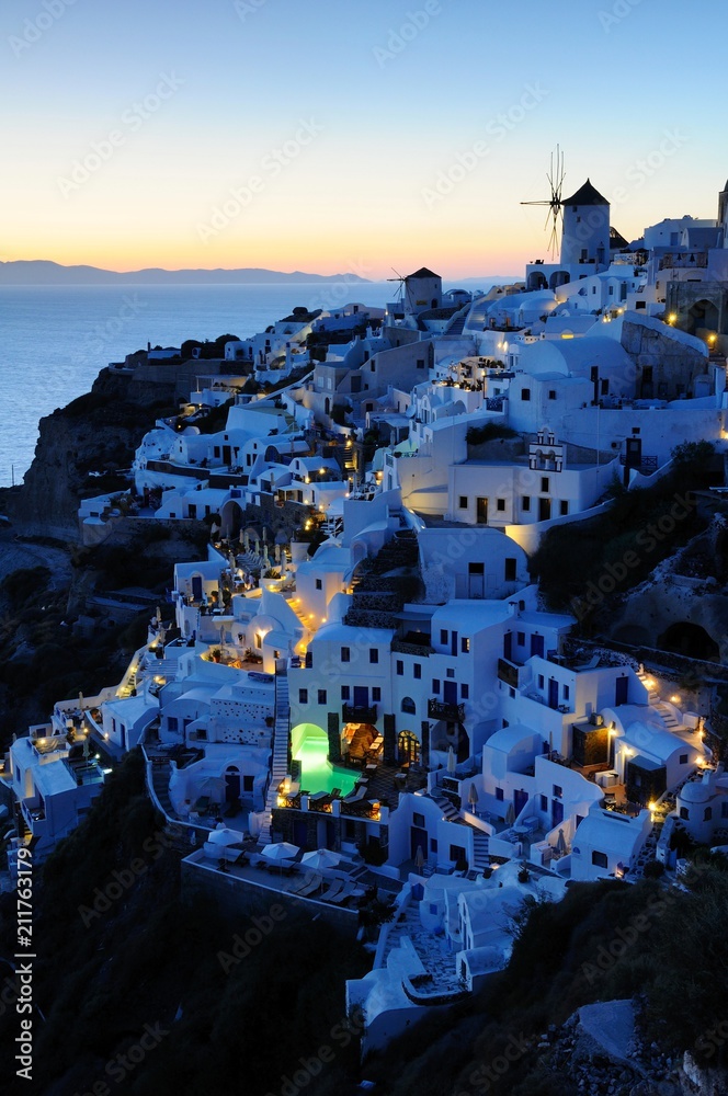 Famous sunset view known as best sunset in the world with white architectures and windmills above the volcanic caldera in the village of Oia in Santorini island, Greece